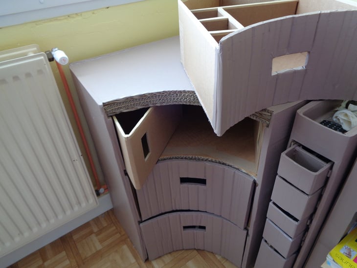 Un meuble d'angle en carton, avec des tiroirs sur -mesure. A coté, il y a un petit rangement, avec des tiroirs, pour les affaires de couture